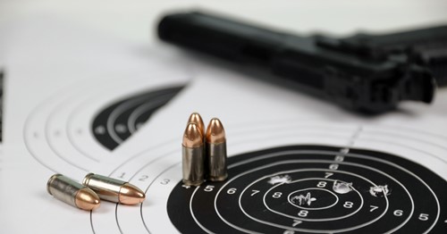 Paper target with gun and bullets in the background