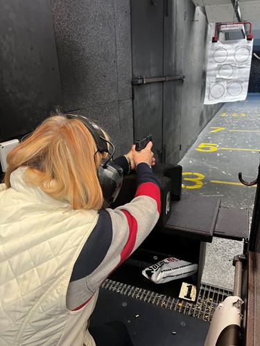 Woman practicing handgun shooting at an indoor range with proper stance and safety gear
