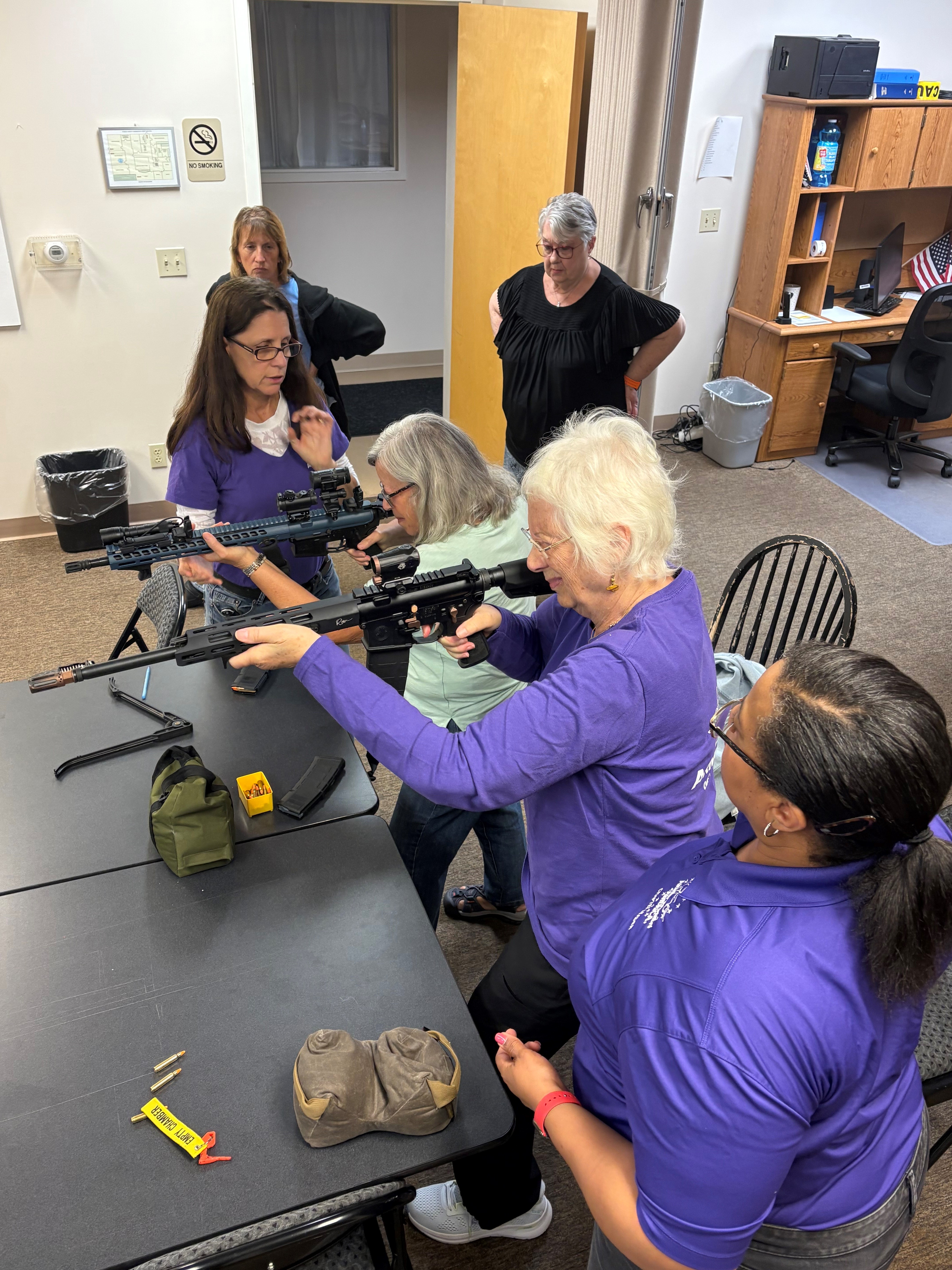 Female firearms instructor guiding women through hands-on rifle training in a classroom setting